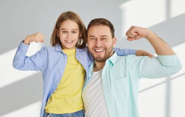 Mutlu baba ve küçük oğul güçlerini ve bağlarını göstermek için kaslarını esnetirler. Sıradan tişörtler ve tişörtler giyen beyaz bir adam ve çocuk pazılarını gösteriş için can atıyorlar. Babalar Günü konsepti.