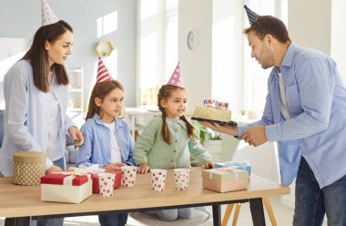 Pastalı mutlu aile doğum günü partisi, komik parti şapkaları giyen aileler ve çocuklar, tebrikler, hediye ve hediye, heyecanlı çocuklar gülüyor ve evde eğleniyorlar, sürpriz yapıyorlar. 