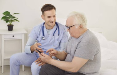 Üst düzey hasta cep telefonunda tıbbi uygulama kullanmayı öğreniyor. Tombul yaşlı bir adam ve önlüklü genç bir doktor. Steteskoplu. Yatakta birlikte akıllı telefon kullanıyorlar. Sağlık hizmeti kavramı