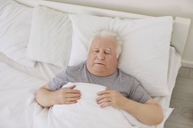 Üst düzey yaşlı, gri saçlı, sabahları yatak odasında uyuyan, beyaz battaniyeyle kaplı bir adamın portresi. Emekli erkek içeride dinleniyor. Yatakta yatıyor..