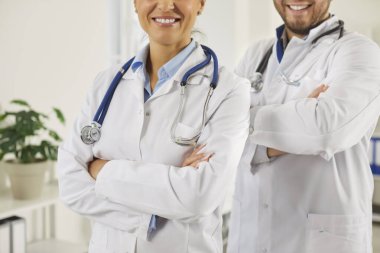 Kollarını kavuşturup kameraya bakan beyaz üniformalı genç doktorlardan oluşan mutlu bir ekip portresi. Klinikte çalışan tıbbi personel. İlaç ve sağlık hizmetleri kavramı.