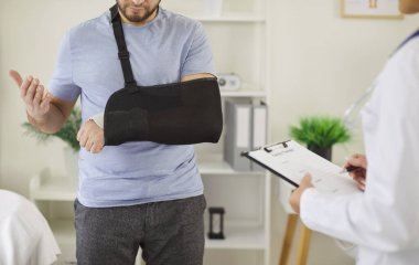Doktor travmatolog muayenehanede kolu kırık el teli takan hastayı muayene ediyor. Eli yaralı biri klinikte muayene oluyor. Tıp ve travmatoloji kavramı.