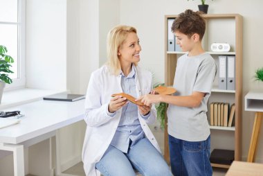 Klinikteki bir uzman bir çocuğa ortopedik taban gösteriyor, yakın plan. Bir çocuk için rahat bir taban seçmek. Konsept doktor çocuk sohbeti, düz taban, hekim danışmanlığı