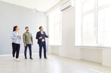 Genç ve mutlu bir çifte güzel bir ev gösteren bir emlakçı. Profesyonel emlakçı parlak yeni bir daire gösterdi. Başarılı bir aile ev sahibi olmaya hazır. Emlak piyasası kavramı.