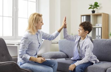 Başarılı terapi seansından sonra gülümseyen küçük çocuk terapiste ya da okul psikoloğuna beşlik çakıyor. Ofiste çocukla çalışan kadın psikoterapist. Çocukların zihinsel sağlık konsepti.