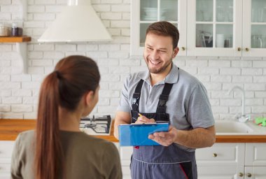 Erkek tesisatçı, kadın müşteriyle konuşuyor. Evde tesisat hizmeti için kontrat imzalıyor. Erkek tamirci ya da tamirci kadın müşteri mutfakta bekliyor. Bakım ve onarım servisi.