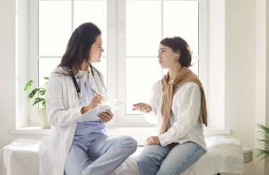 Genç kadın pratisyen hekim hasta ile konuşuyor, reçeteyi, sağlık taramasını, muayene sonuçlarını, konsültasyonu, doktor muayenesini, kanepeye oturan kızı, her şeyi açıklamaya çalışıyor. 