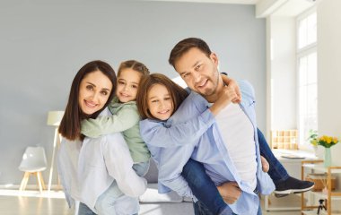 Mutlu, gülümseyen anne ve baba, evde poz veren iki küçük çocuk, kameraya bakan aile, şefkatli bakımın tadını çıkaran aile, gülümseyen ebeveynler, anaokulu çocuklarının birlikte eğlenmesi.