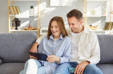 Heyecanlı, mutlu, mutlu aile çifti tablet bilgisayar kullanıyor, haber sunuyor, internette başarılı bir şekilde sohbet ediyor, mal alıyor, internetten hizmet alıyor, e-alışveriş sitelerinde sörf yapıyor, hafta sonu dinleniyor.