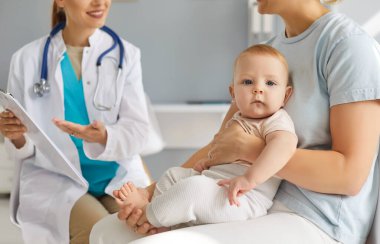 Genç anne ve babası, tatlı bir bebekle oturuyor ve klinikte danışmanlık yapan ve tıbbi muayeneden sonra tavsiyelerini dinleyen gülümseyen dost canlısı çocuk doktoru aile doktoruyla konuşuyorlar..