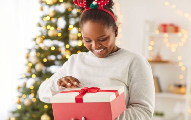 Evdeki oturma odasında elinde kırmızı hediye kutusuyla bekleyen Afro-Amerikan bir kızın portresi. Yeni yıl ve bayram kutlaması konsepti.