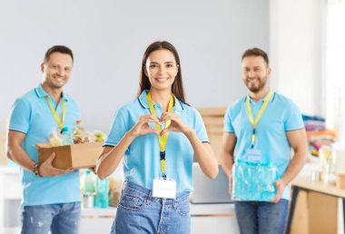 İnsani yardım merkezinde birlikte duran neşeli gönüllü ekibinin portresi. Gülümseyen genç bir kadın ellerinde yiyecek bağışı yapan neşeli erkek meslektaşlarıyla kalp hareketi yapıyor..