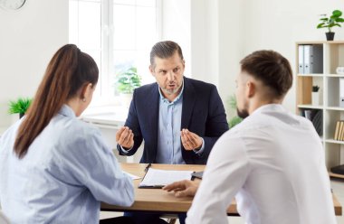 Masada oturan genç çift olgun erkek emlakçıyla ya da mali danışmanla görüşüyor. Ofiste müşterilerle çalışan bir iş adamı ya da sigortacı. Emlak piyasası kavramı.