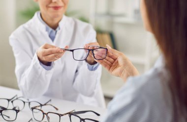 Bir doktor oftalmolojistin yakın çekimde gözlüğü hastanede bir hastaya verirken, tıbbi göz bakımı ve profesyonel sağlık hizmetlerinin önemini vurguluyor..