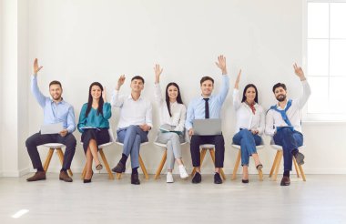 Bir grup iş adamı, bir ofis toplantısı sırasında soru sormak için el kaldırıyor. Takım birlikte çalışıyor, aktif katılım, işbirliği ve iş ortamında iletişim gösteriyor.