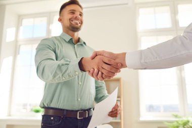 Memnun iş adamı ofisteki memnun bir müşteri veya meslektaşına el sıkışır. Bu sembolik jest başarılı bir anlaşma, ortaklık ya da etkin takım çalışmasının doruk noktası..