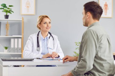 Ciddi gülümseyen kadın doktor, sağlık muayenesi sonuçlarını klinikteki erkek hastaya açıklıyor. Konuşuyor, hastane toplantısı sırasında muayene yapıyor ve destek veriyor.