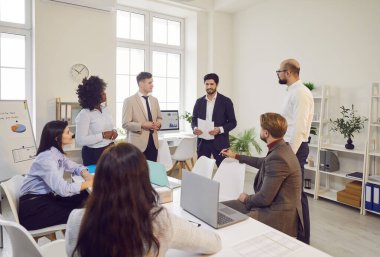 Ofisteki bir grup çok kültürlü iş adamı bir meslektaşının raporunu dinliyor. Erkek çalışanın elinde bir belge var. Meslektaşları ona bakıyor. Kavram gündemi, takım çalışması