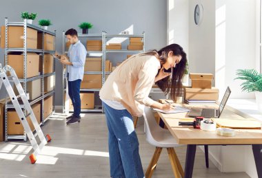 Çevrimiçi küçük bir mağazada çalışan insanlar. Depoda çalışan meşgul kadın ve erkek çalışanlar raflarında karton kutular var. E ticaret, lojistik, KOBİ envanter yönetim kavramı