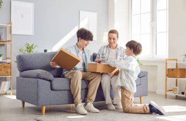 Genç mutlu anne ve baba, çocuklarıyla birlikte oturma odasında paketleri açıyor ve açık karton kutuya bakıyor. Teslimat, online alışveriş, paket konseptini al.