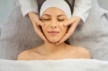 Güzellik salonundaki güzellik uzmanından yüz masajı yaptıran ve güzellik tedavisi gören mutlu, genç ve güzel bir kadının portresi. Refah kavramı.