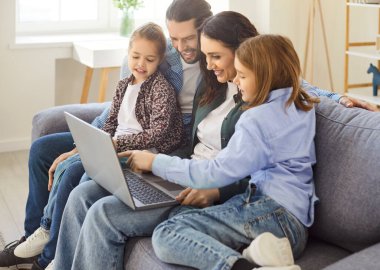 Çevrimiçi eğlence için dizüstü bilgisayar kullanan neşeli bir aile. Mutlu ve evde dinleniyor, birlikte vakit geçiriyoruz. Rahat bir atmosferde internet eğlencesi ve dijital aktiviteler.