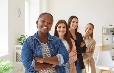 Mutlu bir Afro-Amerikalı iş kadınının portresi. Ofiste kadın takımıyla güvenle ayakta duruyor. İş grubu işbirliği, çeşitlilik ve profesyonel başarıyı somutlaştırıyor.