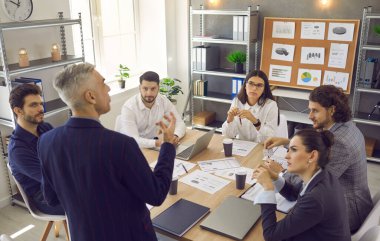 Kıdemli deneyimli bir işletme yöneticisi, çalışanlarına modern bir ofisteki toplantıda talimat verir. İnsan konuşur, işi tartışır ve çözümler sunar. İş başarısı konsepti.