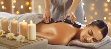 Rahatlamış esmer kadın sağlık merkezinde sıcak taş masajı yaptırıyor. Güzel sakin kız kanepede uzanıp güzellik salonunda vücut tedavisinin tadını çıkarıyor. Güzellik terapisi, vücut bakımı konsepti.