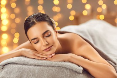 Güzellik salonunda rahatlayan genç bir kadının portresi. Güzel esmer kız gözleri kapalı uzanmış masaj ve spa ameliyatının tadını çıkarıyor. Güzellik, sağlık, vücut bakımı konsepti