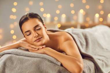 Genç, güzel bir kadın, masaj koltuğunda çıplak ve gözleri kapalı uzanıyor. Spa sırasında dinleniyor. Sağlık tedavisi gören bir kız. Sağlık ve güzellik günü konsepti.