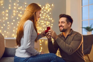 Benimle evlenir misin? Birbirine aşık çiftler evde romantik bir akşam geçiriyorlar. Evlilik teklifi alan ve kabul eden mutlu genç bir kadın. Gülümseyen adam kız arkadaşına evlenme teklif ediyor ve ona nişan yüzüğü veriyor.