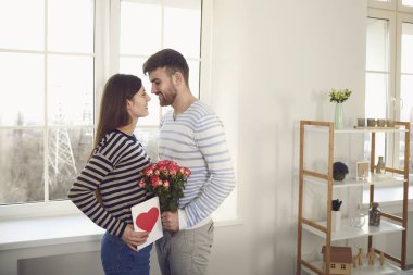 Sevgililer Günü. Adam, odadaki kanepede oturan bir kıza kırmızı kalpli bir sevgililer günü kartı veriyor..