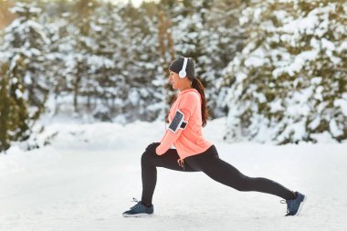 Genç bir kadın kışın karda antrenmandan önce ısınır..