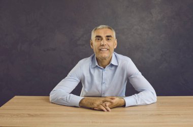 Orta yaşlı, gülümseyen beyaz bir adamın portresi siyah arka plan konuşmasında masada oturuyor ve video konuşmasında konuşuyor. Mutlu erkek kameraya bakar müşteri veya müşteri ile sanal sanal iletişim kurar.