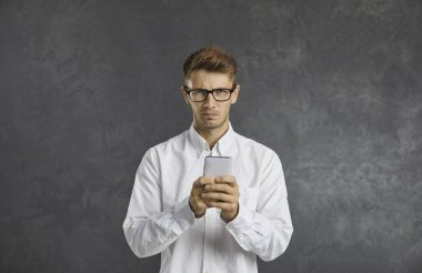 Yavaş internetten rahatsız olan ya da spam mesajı alan memnuniyetsiz bir adamın portresi. Kızgın bakışlı beyaz bir adam gri arka planda duran kameraya bakar..