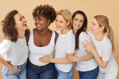 Kadın günü. Çok uluslu bir grup farklı ve mutlu kadın birlikte gülüyor, bej bir arka planda duruyorlar. Kadınlık, güzellik ve farklı kültürlerden kadınlar arasında paylaşılan anların neşesi..