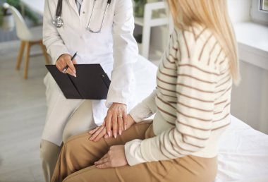 Beyaz önlüklü bir doktorun elini tutup duygusal destek sunduğu bir sahne. Konsültasyon sırasında empati ve şefkat gösteren, dikkatle dinleyen bir doktor..