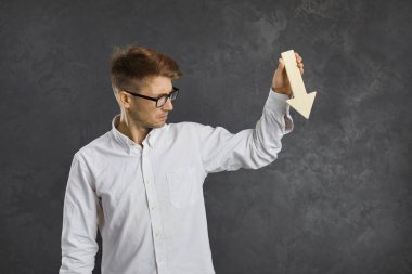 Grafik çizelgesini tutarak para kaybeden tüccar ya da işyeri sahibi gri arka planda izole edilmiş bir yeri işaret ediyor. Mutsuz genç adam kar azalması, bütçe kesintileri, devalüasyon veya kötü performans yaşıyor