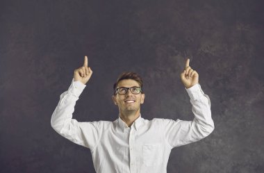 Neşeli adam işaret parmağıyla işaret ediyor. Yazı için boş alana bakarak neyi seçeceğini söylüyor. Gri duvarın arka planında neşeli beyaz bir adam. Halk ve tanıtım konsepti.