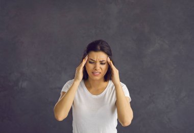 Şakaklarına dokunan endişeli genç bir kadının portresi şiddetli baş ağrısı ve stres hissediyor. Kafkasyalı esmer kadın acı ve migren yüzünden umutsuzluğa kapılmış. Sağlık sigortası konsepti. Gri arka plan. Stüdyo çekimi