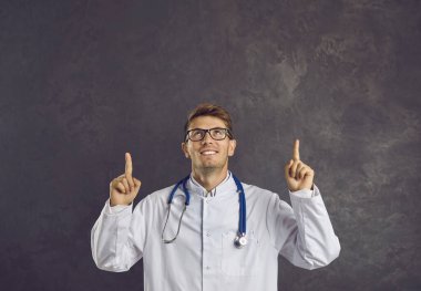 Gülümseyen genç bilim adamı ya da beyaz önlüklü doktor, siyah stüdyo arka planında izole edilmiş boş fotokopi alanını gösteriyor. Mutlu adam pratisyen hekim iyi bir terfi ya da ilaç satış anlaşması öneriyor..