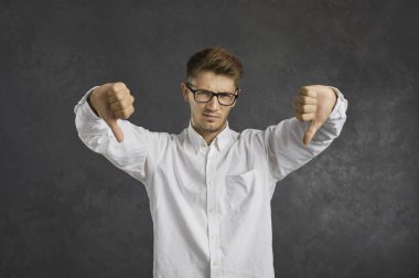 Bu ezikçe. Hayır, hiç hoşuma gitmedi. Etkilenmedim. Kötü bir fikir. Hoşnutsuz genç adamın el hareketlerinden hoşlanmadığı bir fotoğraf stüdyosu. Gri arka planda tek başına duran etkilenmemiş bir adamın baş parmağını geri çevirmesi