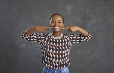 Dişçisine gittikten sonra gülümseyen genç bir kadın. Gri stüdyo arka planında duran mutlu kısa saçlı siyahi kadının portresi mükemmel beyaz dişli güzel gülüşünü işaret ediyor.