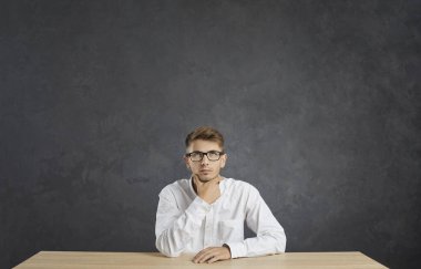 Yansımalar. Ciddi bir beyaz adamın portresi. Gri arka planda dalgın bir ifade var. Tişörtlü ve gözlüklü bir adam masaya oturmuş önemli şeyler düşünüyor ya da karar veriyor..