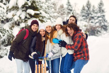 Arkadaşlar kameraya gülümsüyor ellerinde kızaklarla kışın karların üzerinde