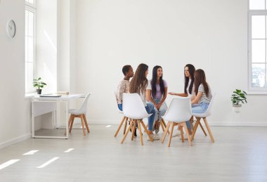 Grup terapisi sırasında tartışan mutlu genç kadınlar. Olumlu gülümseyen çok ırklı kızlardan oluşan bir ekip geniş beyaz ofis odalarında daireler çizerek otururken yaşam tarzı koçuyla konuşuyor.