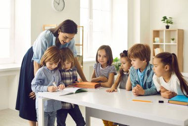 Modern bir ilkokula giden bir grup öğrenci. Gülümseyen genç Kafkas öğretmeni ders sırasında çocukların resim yapmasını izliyor. Sınıftaki öğrenciler masanın etrafında duruyorlar..