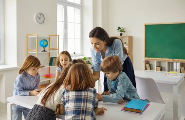 Sınıfta çocuklara ders veren beyaz bir öğretmen ya da anaokulu öğrencileri konuşuyorlar ve görevlerini gösteriyorlar. Eğitim ve öğrenim, ilkokul ya da anaokulu çocuk gelişimi