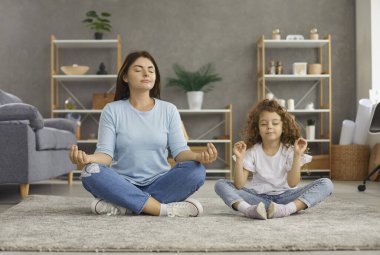 Sakin, genç, beyaz bir anne ve 7 'nin kızı Mudra elleriyle yerde oturup meditasyon yaparak negatif duyguları hafifletiyor. Rahatlamış anne ve küçük kız çocuk istirahati birlikte yoga yapıyorlar. Stressiz konsept.